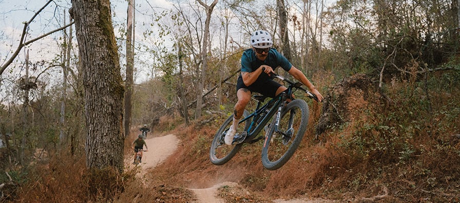 Mountain biker wearing smith bike helmet and sunglasses jumps over a bump while shredding some single track