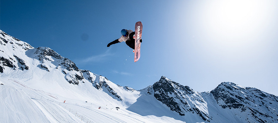 Snowboarder sending a big jump while grabbing their board with blue skies and a mountain range in the background